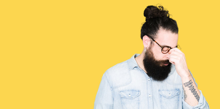 Young hipster man with long hair and beard wearing glasses tired rubbing nose and eyes feeling fatigue and headache. Stress and frustration concept.