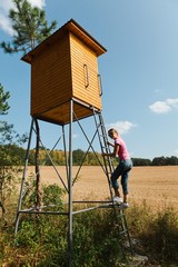 Woman climbing on high seat for hunters.