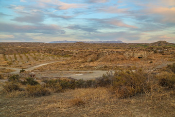 a path leads through a ruff steppe grassland landscape with hills and blue light cloudy colorful sky