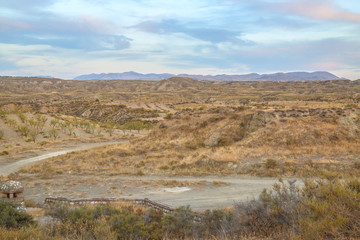 Fototapeta na wymiar a path leads through a ruff steppe landscape with hills and blue light cloudy sky