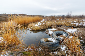 Two used ejected big tires in the water of the grassland river at the wintertime