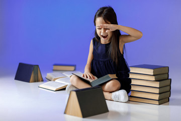 cute tired little girl in dark blue dress is reading a book. child and a lot of books. Children and education.