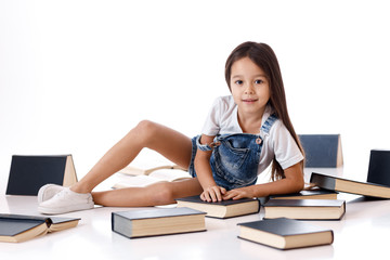 cute little girl in denim is reading a book. child and a lot of books. Children and education.