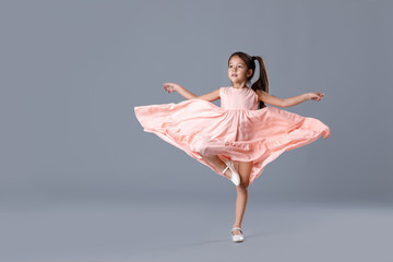 cute little ballerina girl in pink dress dancing on gray background.