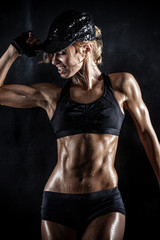 beautiful athletic woman in cap posing on dark