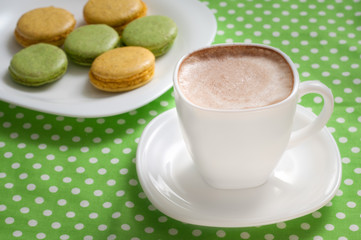 A cup of cappuccino and a plate of macaroons on the table.