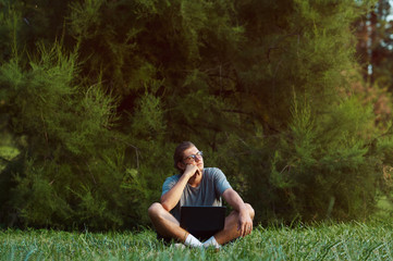 Obraz premium A young handsome male with notebook outside. Serious confident boy thinking about future while sitting on grass in public park.