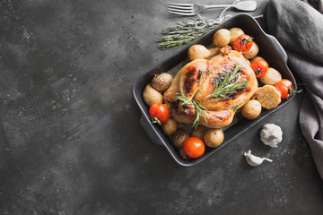Roasted chicken with vegetables on black table.