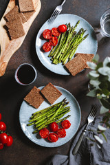 View from above on dinner for two people, grill asparagus and cherry tomatoes. Vegetarian food.