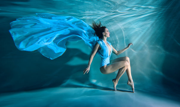 Girl portrait posing underwater in blue fashion dress in swimming pool alone in the deep