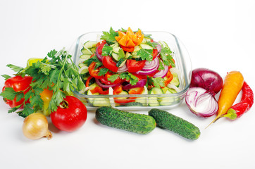 Fresh vegetable salad in a salad bowl and its ingredients on a white background. Tomatoes, cucumbers, onions, garlic, parsley.