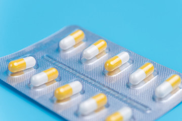 Medicine white and yellow pills packed in blisters on blue background