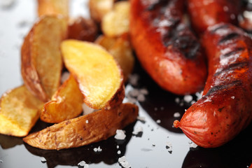 Grilled sausages.Baked potatoes .Closeup.On miroor surface.Tasty dish