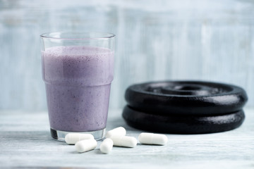 Glass of Protein Shake with milk and blueberries. Creatine capsules and plates in background. Sport nutrition. rustic Wooden background. Copy space. 