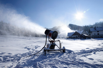 Landscape of a mountain ski resort, where slope are prepare by snowmaking machine with artificial white snow. Footsteps in deep snow cover. Mountain and houses in the background. Winter holidays.
