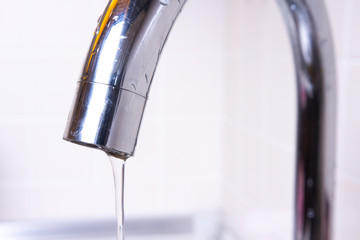 Jet of water pouring from tap. Faucet with water drop close-up
