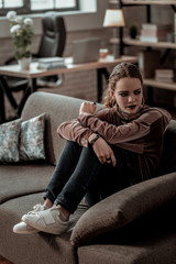 Teenager wearing jeans and sneakers sitting on sofa at home