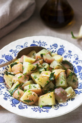 Traditional cold potato salad with onions and herbs on a linen tablecloth background. Rustic style.