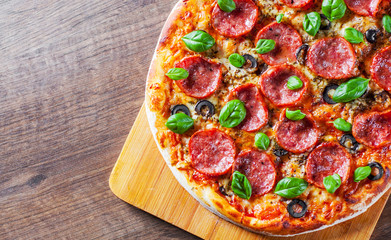 Pepperoni Pizza with Mozzarella cheese, salami, Tomatoes, olive, pepper, Spices and Fresh Basil. Italian pizza on wooden table background