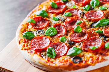 Pepperoni Pizza with Mozzarella cheese, salami, Tomatoes, olive, pepper, Spices and Fresh Basil. Italian pizza on wooden table background
