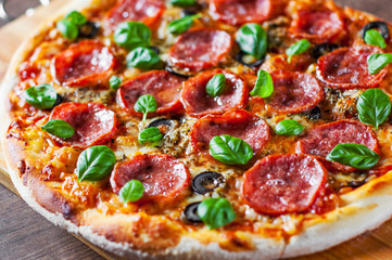 Pepperoni Pizza with Mozzarella cheese, salami, Tomatoes, olive, pepper, Spices and Fresh Basil. Italian pizza on wooden table background