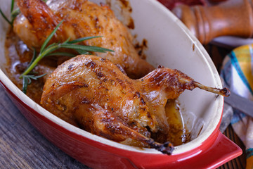 Delicious baked quails in a ceramic roasting pan on a wooden table prepared for a delicious lunch or dinner