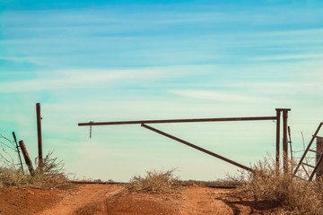 Grungy old iron gate to pasture over cattle guard with blue-turquoise sky and red earth and winter weeds - Western Oklahoma