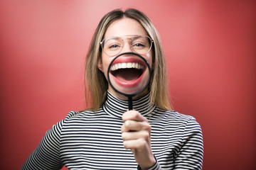 Funny young woman showing her mouth trought magnifying glass over pink background.