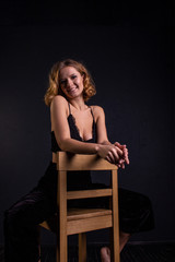 Fototapeta premium A pretty woman with a good figure is standing in a bra and black pants near the bar stool in the room.