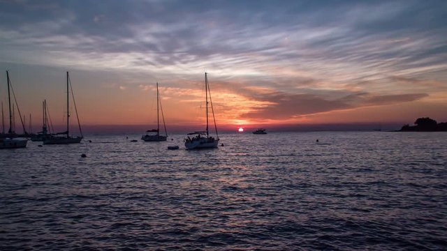 Many siling boats are standing on the sea and the sun is going down