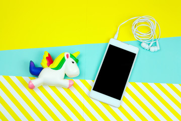 top view unicorn and smartphone with earphones on a bright blue and stripped yellow background