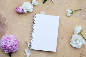 Open notebook with flowers and black coffee on beige background. Flat lay. Top view. Copy space.
