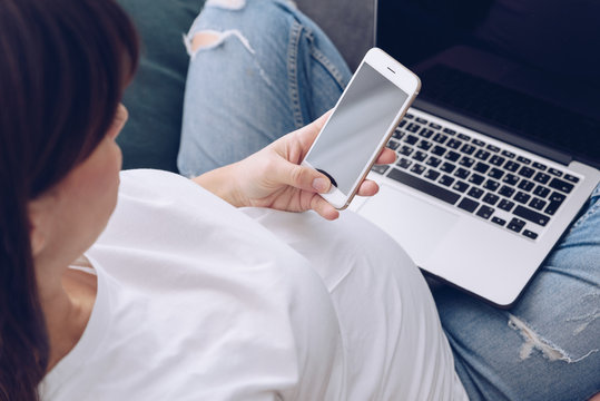 Young pregnant woman is working on laptop at her home, makes a call