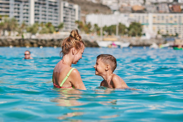 Fototapeta na wymiar Mom and son are splashing in the ocean, they are happy to spend holidays together.