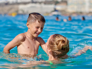 Mom and son are splashing in the ocean, they are happy to spend holidays together.