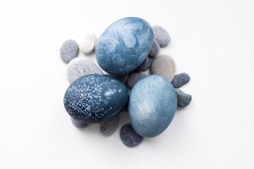 Three colored blue, gray marble eggs lie on the stones on a white background