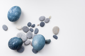 Three colored blue, gray marble eggs lie on a white background among the stones