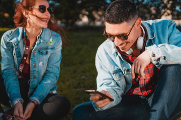 Happy young couple in love using smartphone while sitting in a green park