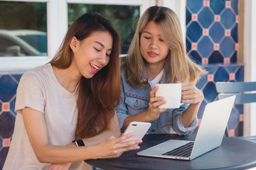 Asian young women working on laptop using and looking smartphone and drinking coffee while sitting in cafe. Lifestyle women communication and working in coffee shop concept.