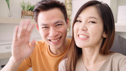 Asian couple using smartphone VIDEO Call with friend in living room at home, sweet couple enjoy love moment while lying on the sofa when relaxed at home. Lifestyle couple relax at home concept.