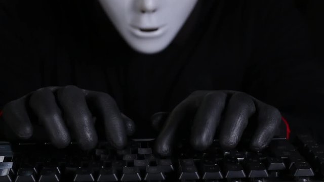 Masked Character Hacker Typing on a computer keyboard wearing gloves