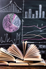 Books on the table against the background of a chalkboard on which are drawn graphs and charts of...