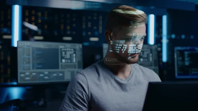 Portrait of Young Software Developer Working on Computer in Digital Identity Cyber Security Data Center, Projected Program Coding Language Reflects on Face. Futuristic Hacking and Programming Concept