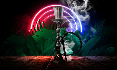 Hookah on a background of tropical leaves on a wooden table, night view, neon lights of the night.