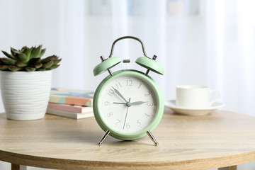Beautiful retro alarm clock with cup of coffee, succulent plant and books on table against light background