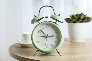 Beautiful retro alarm clock with cup of coffee and succulent plant on table against light background