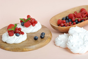 Meringue with fresh berries raspberries, blueberries and red currants. The dessert is decorated with mint leaves. In the frame of a bowl of berries. Light background. Close-up.