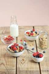 The concept of a healthy breakfast. Granola with berries, with milk and cutlery. Light wooden background. Vertical frame orientation. 