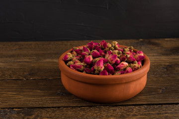 tea rose buds in a  clay pot on the wooden table isolated on black  background