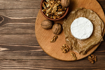 Camembert or Brie cheese with walnut kernels on wooden wooden background. Copy space. white mold grows on top Penicillium camemberti. 